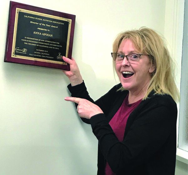 Anna Apoian pointing to her Director of the Year plaque