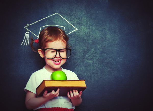 Girl with textbook and apple in front of chalkboard