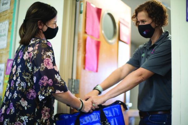 Two women in respiratory masks pass a bag between them