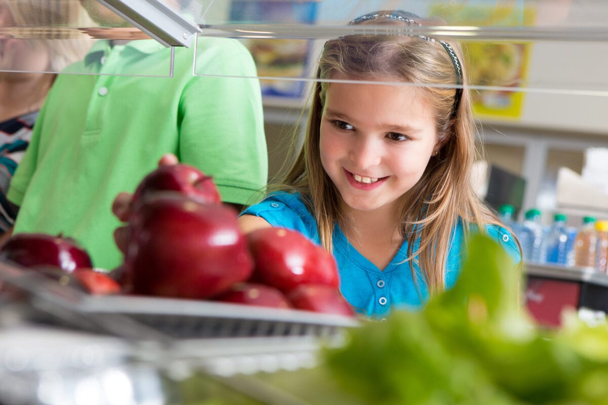 Cute little girl taking apple in school lunch line.