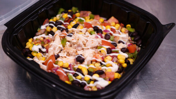 Corn, chicken, tomatoes, black beans and peppers in a black bowl with a white cheese sauce drizzle