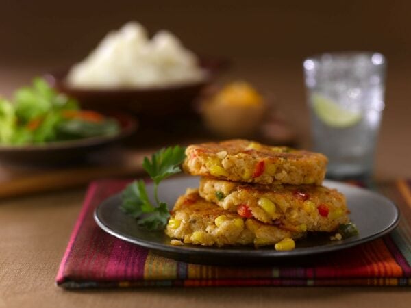 Corn and potato cakes on a black plate with a glass of water in the background