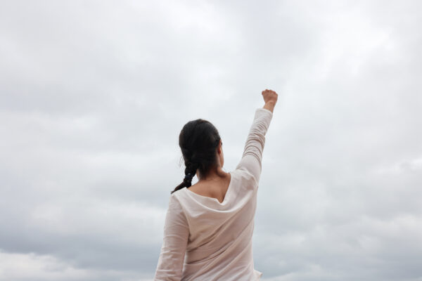 Woman in a white shirt with her fist in the air and back turned