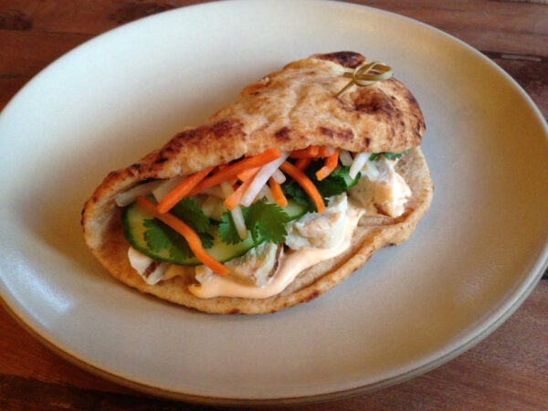 Flatbread filled with Sriracha mayonnaise, chicken, cucumber, shredded carrot and radish and cilantro on a white plate