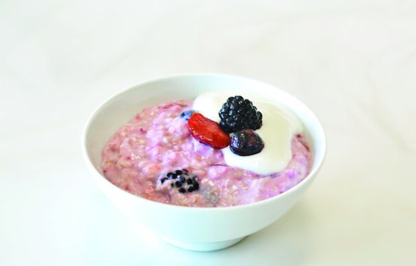 One bowl of pink, berry oatmeal topped with yogurt, two blackberries, two blueberries, and a strawberry slice