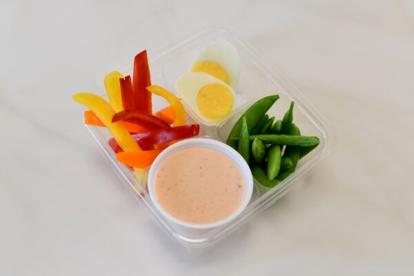 A cup of chili cheese sauce with bell peppers, peas and a hard boiled egg