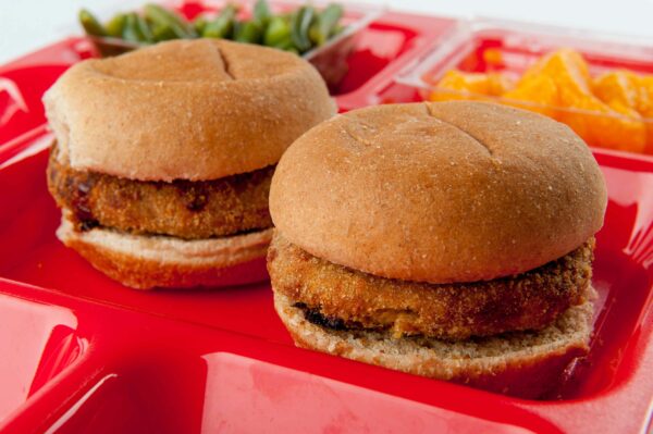 Two sliders on a red tray with green beans and oranges
