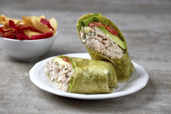 Two wraps with tuna, avocado, tomato and lettuce on a white plate