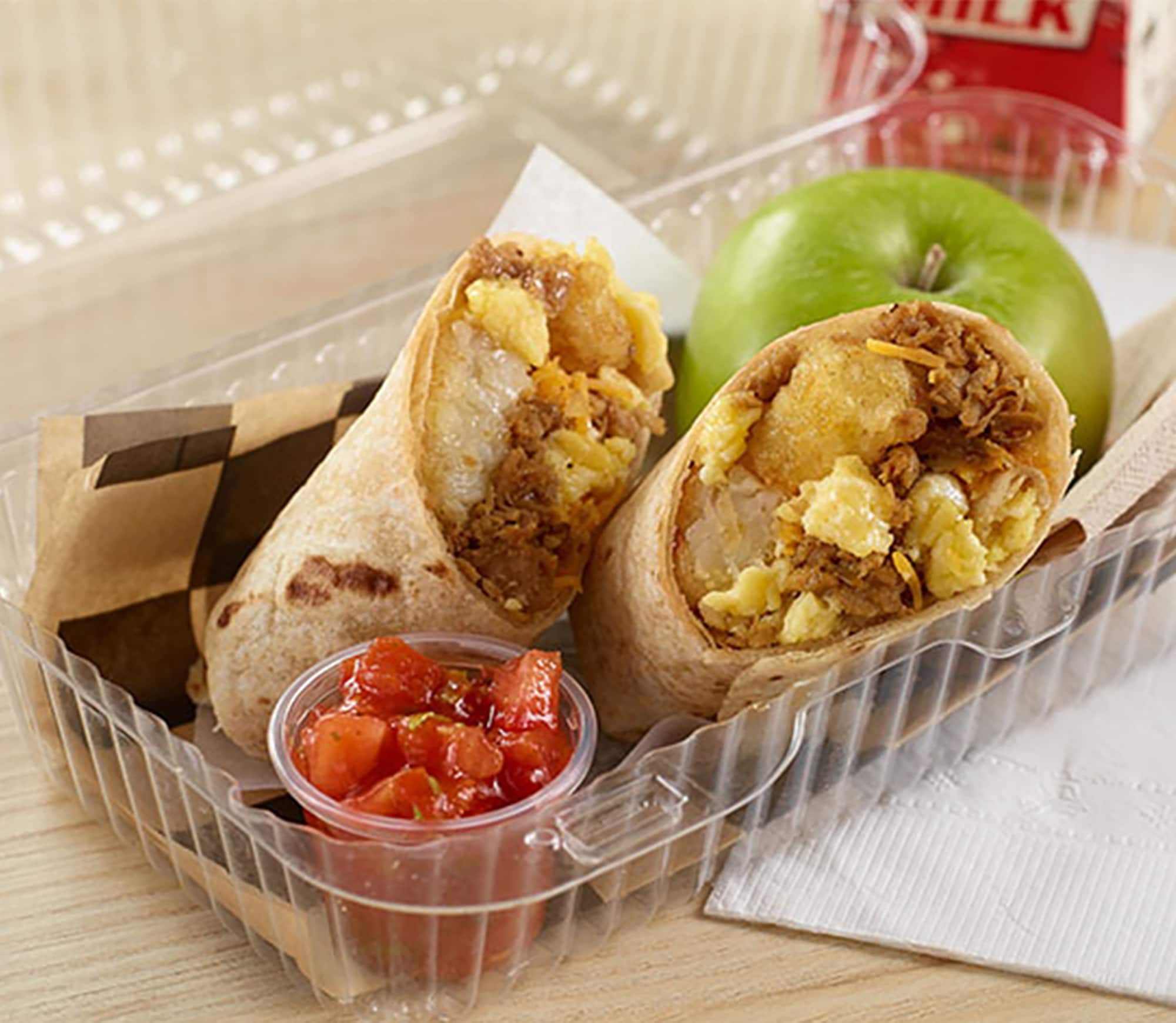 Vegan brunch burrito next to a cup of salsa and a green apple in a plastic clamshell container.