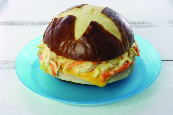 A sandwich with sliced turkey, cheese and coleslaw mix on a pretzel bun