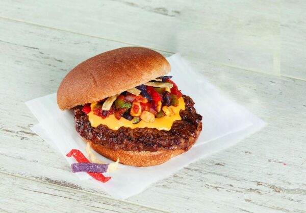 A hamburger patty with nacho cheese, salsa and tortilla chip strips on a bun