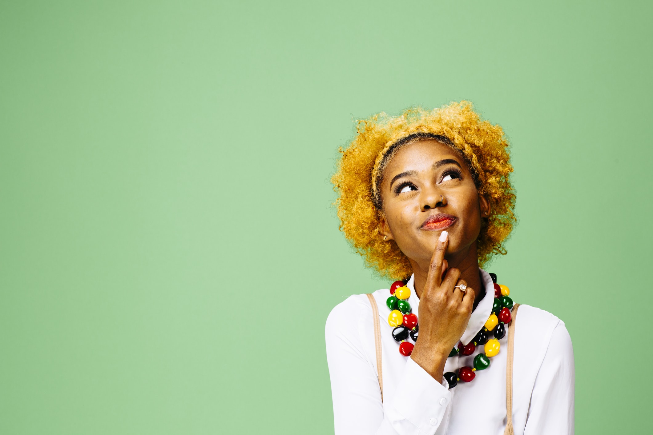 Young woman thinking and looking up, isolated on green studio background