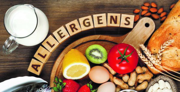 Allergy food concept. Allergy food as almonds, milk, pistachios, tomato, lemon, kiwi, trout, strawberry, bread, sesame seeds, eggs, peanuts and bean on wooden table