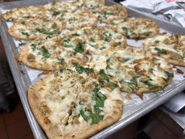 12 small chicken and spinach alfredo flatbread pizzas on a sheet pan