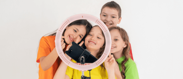 Four children posing behind a ring light and phone, recording a TikTok